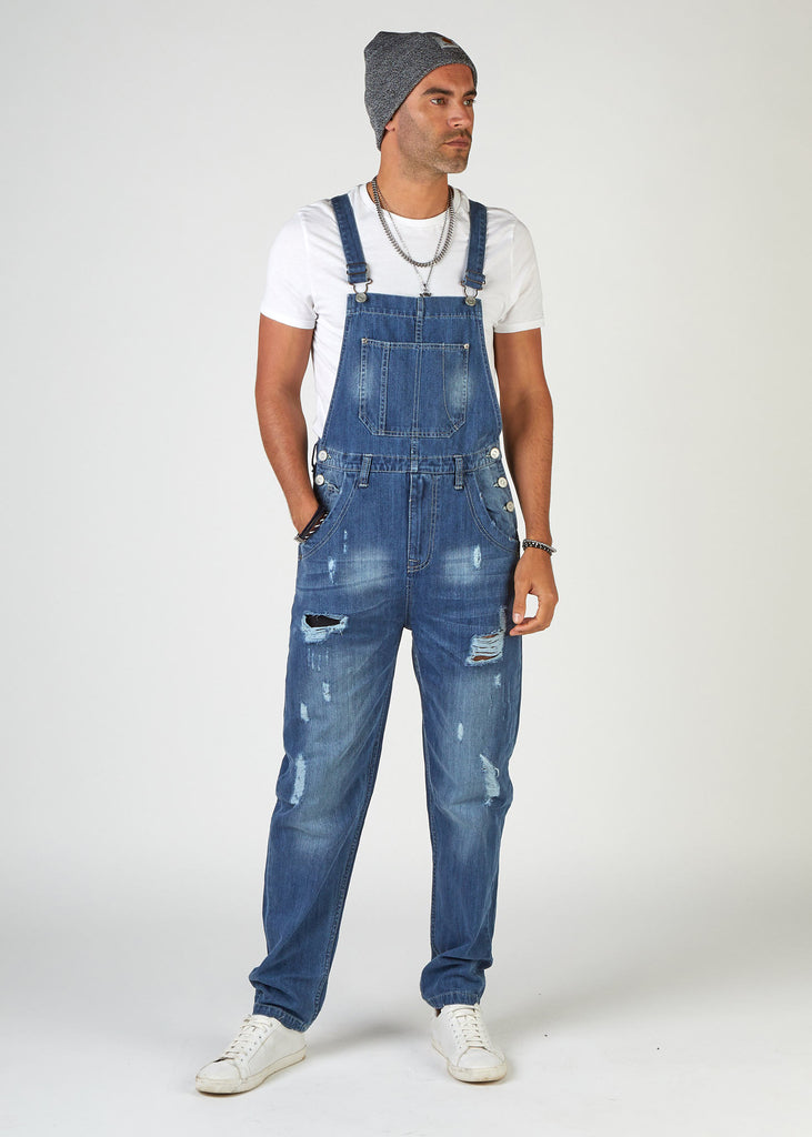 front, full-length pose, looking to model's left, wearing loose, midwash, ripped denim dungarees.
