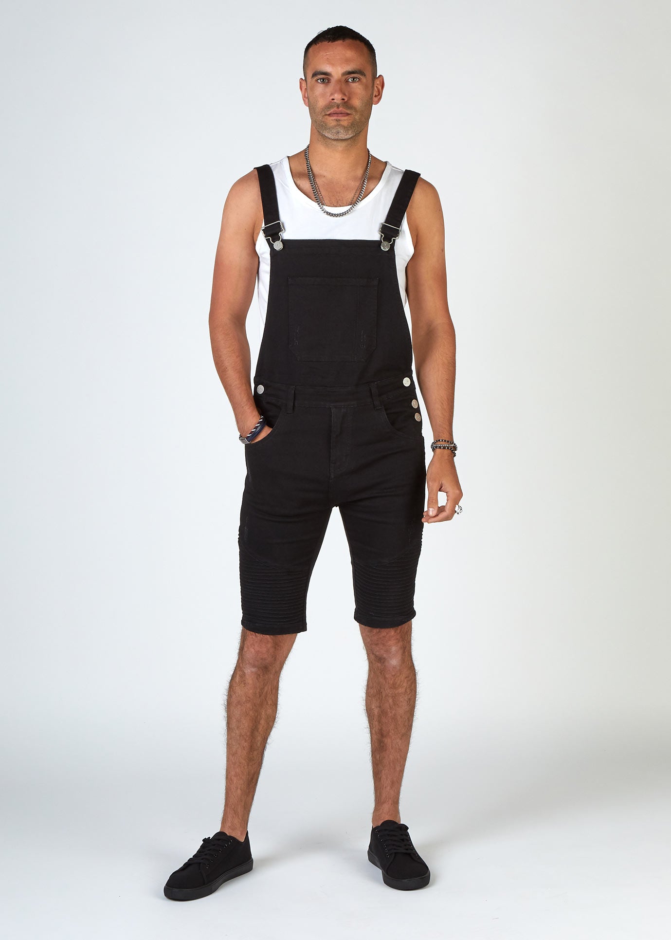 Full-length front shot with male model wearing Trafford skinny black dungaree shorts, a white vest and black trainers