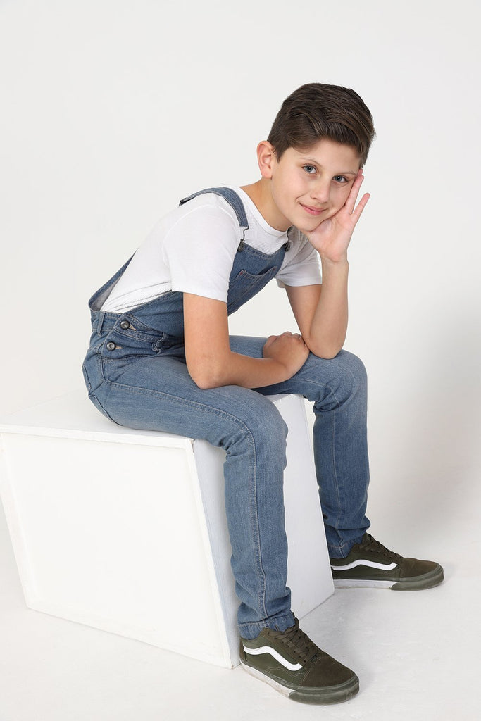 Side-view of boy sitting on box wearing durable, zip fly, machine washable denim dungarees.