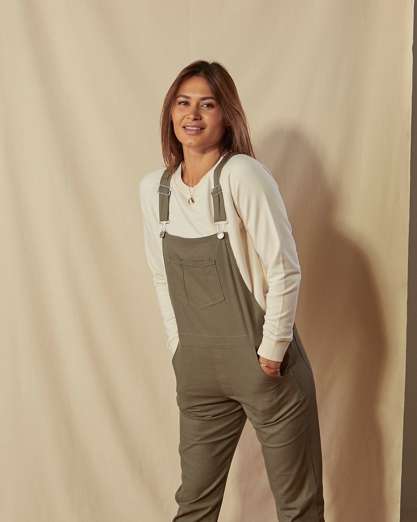 Two-thirds front view of model wearing Harper green organic cotton dungarees with focus on front pockets, bib pocket and adjustable straps.