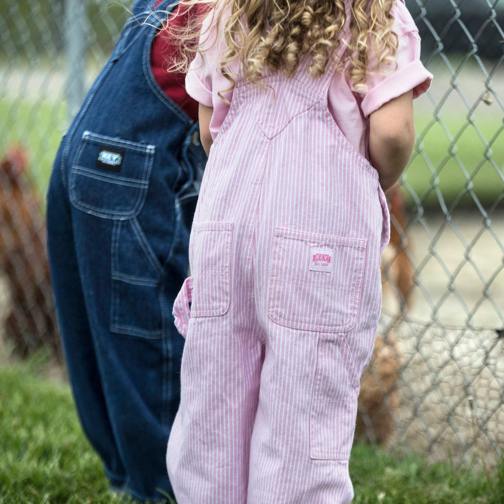 Candid back shot of young girl wearing pink stripe dungarees showing back pockets and key industries USA branding label.