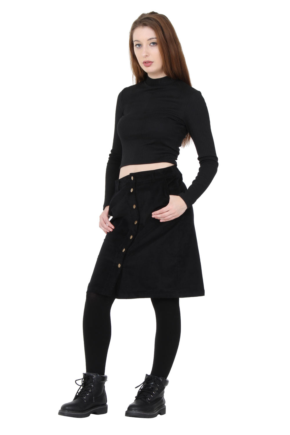 Full-length, slightly angled front view wearing Alice stretch black corduroy knee-length skirt with thumbs in front pockets.