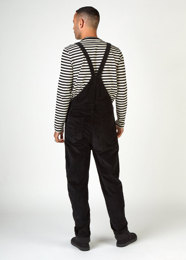 Full-length, back view of model wearing black cord dungarees with clear view of back pockets and belt loops.