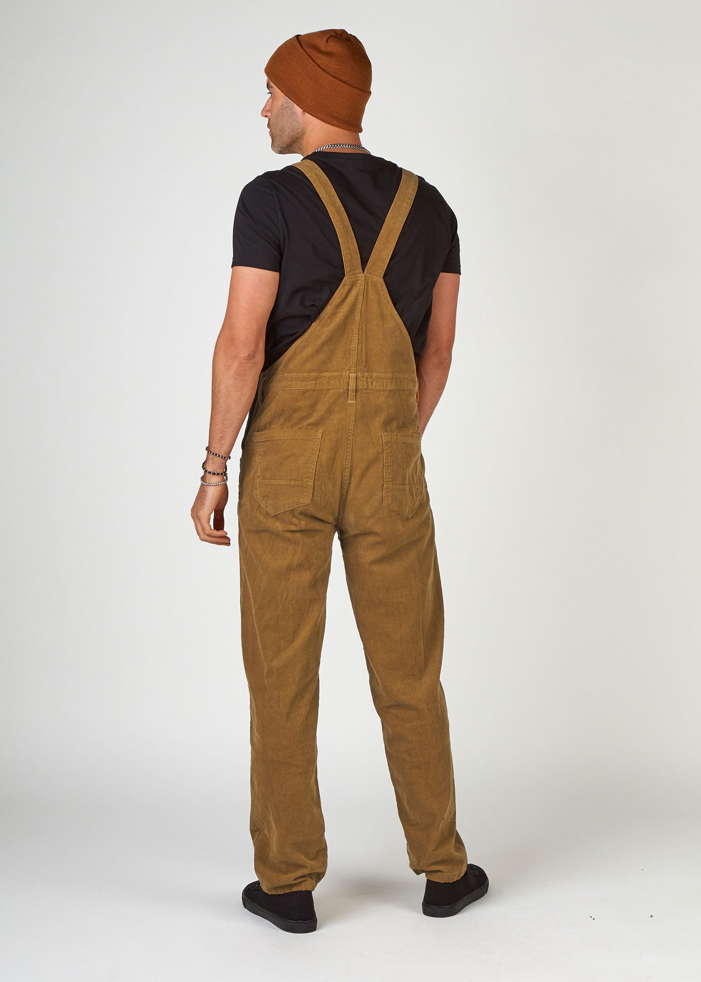 Full-length, back view of model wearing light-brown cord dungarees with clear view of back pockets and belt loops.