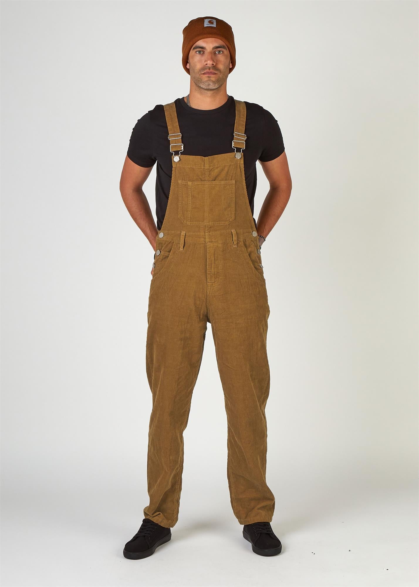 Full-length, front view of model wearing tan corduroy dungarees with clear view of side button fastenings, front and bib pockets. 