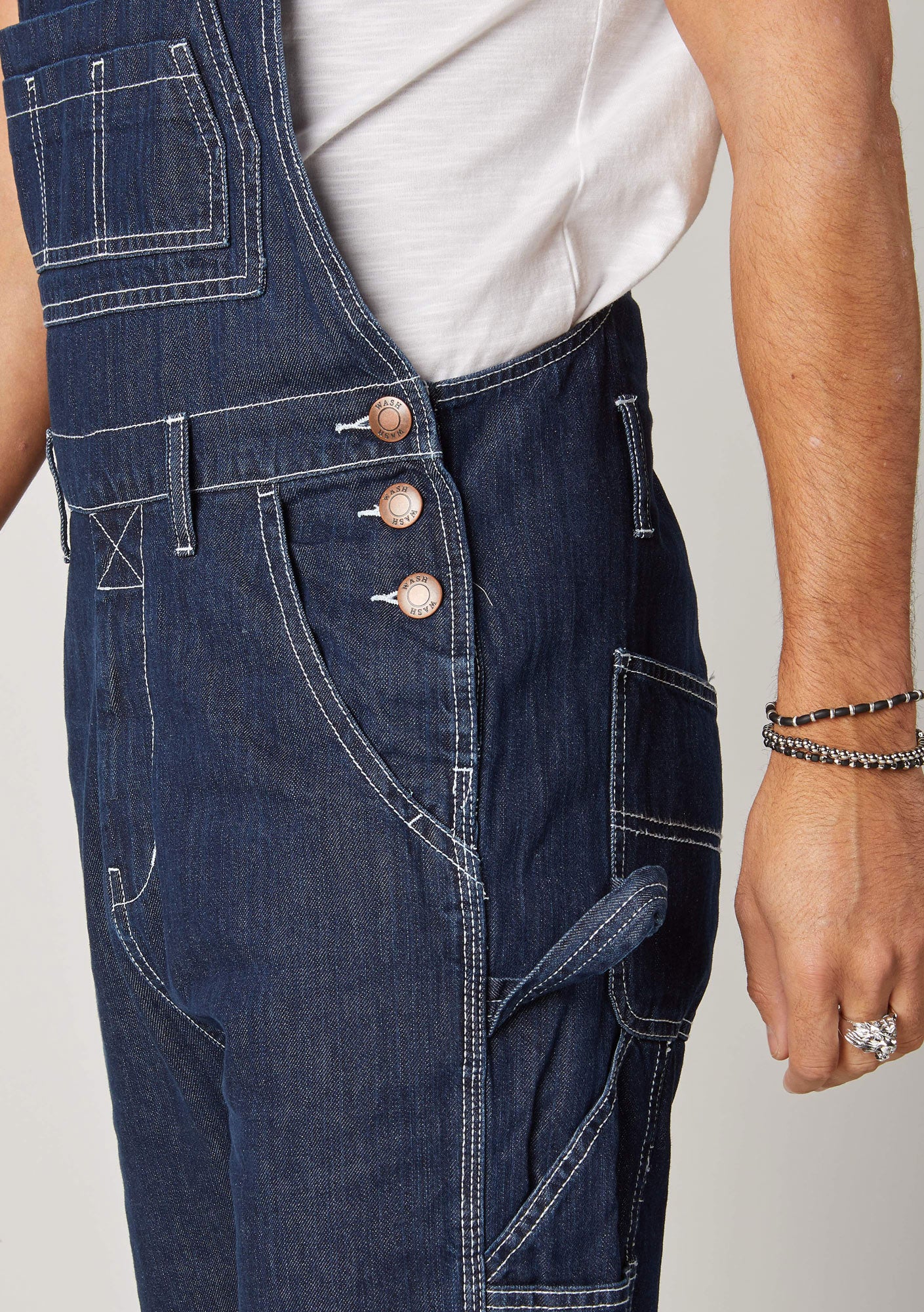 Close-up side pose wearing contemporary 'Maddox' dungarees with view of elegant 3-button fastening, pockets and belt loops.