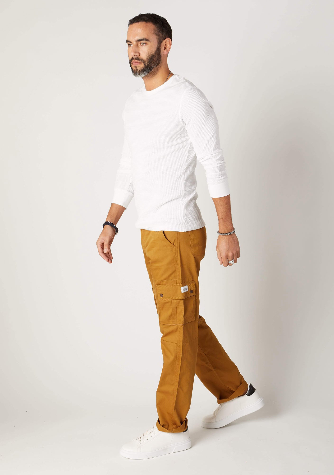 Walking pose, side-view of relaxed fit, organic cotton cargo trousers, with clear view of front cargo pockets.