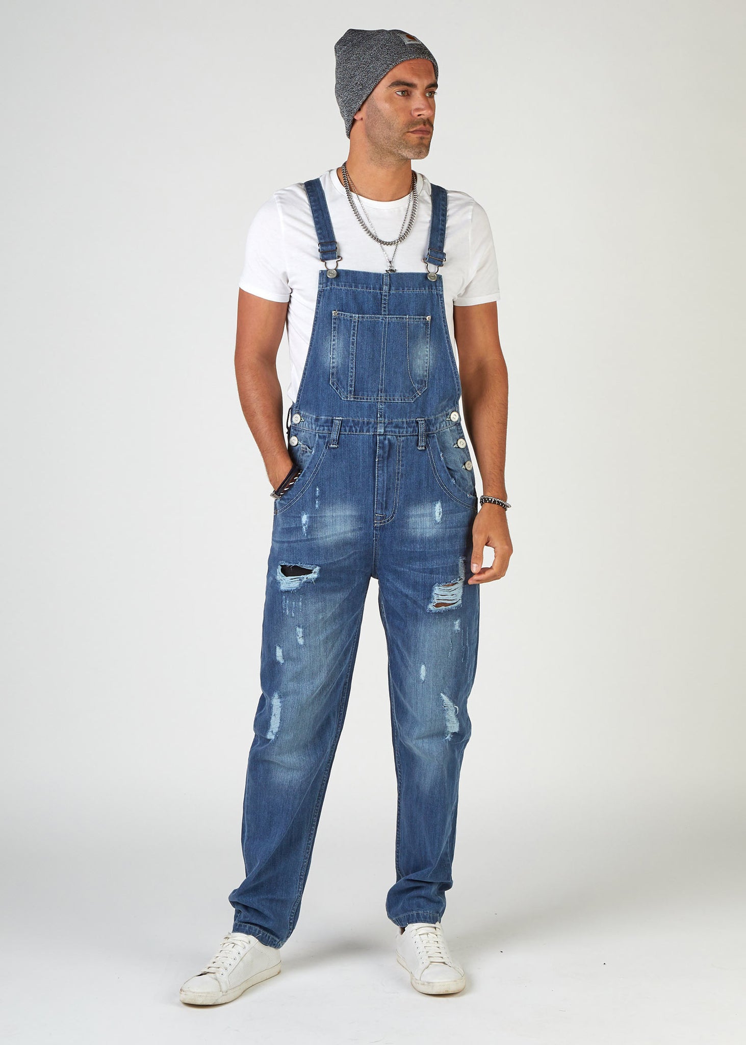 front, full-length pose, looking to model's left, wearing loose, midwash, ripped denim dungarees.