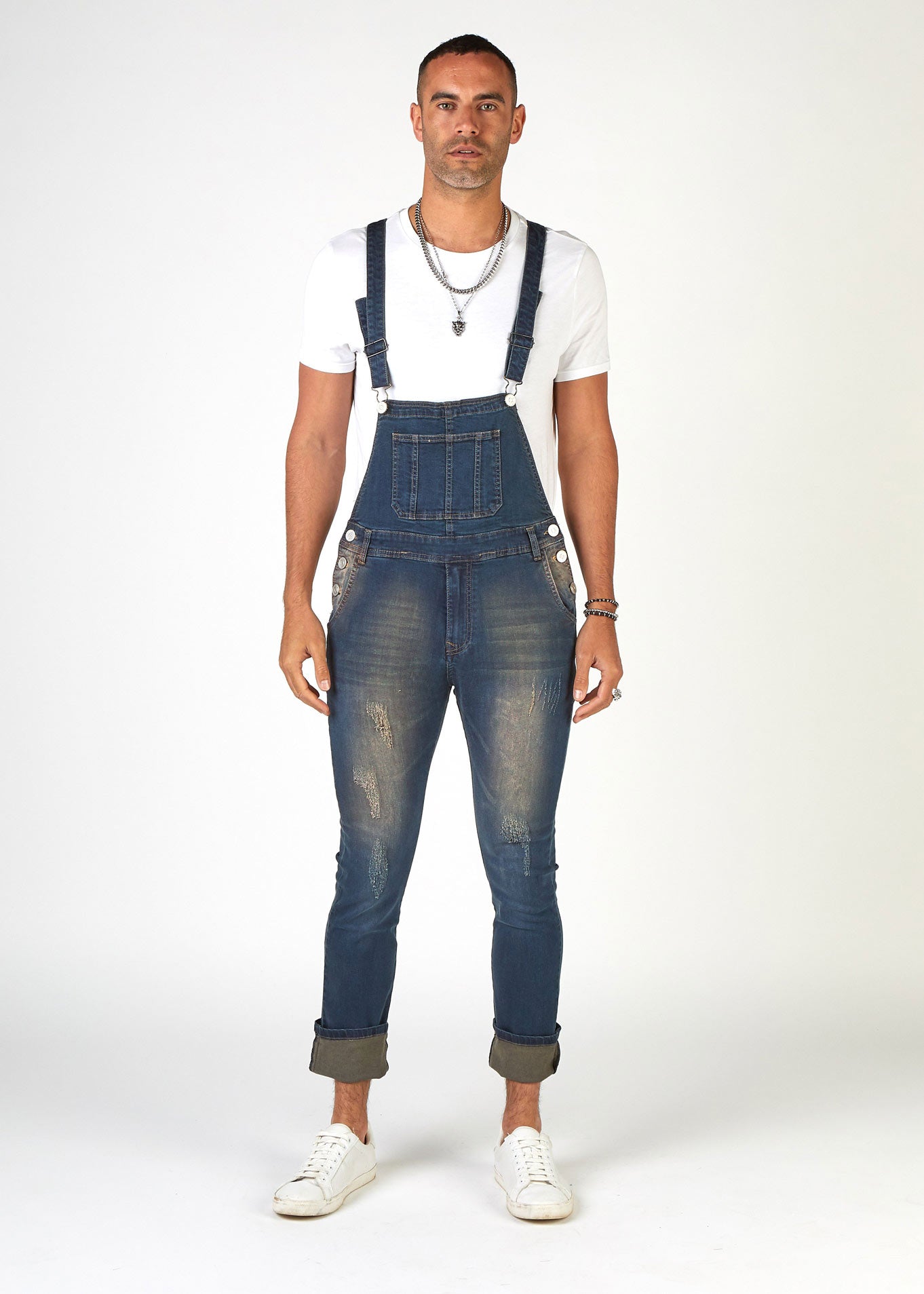 Full-front pose showing skinny fit style of men's denim dungarees with abrasions. Styled with legs turned up.