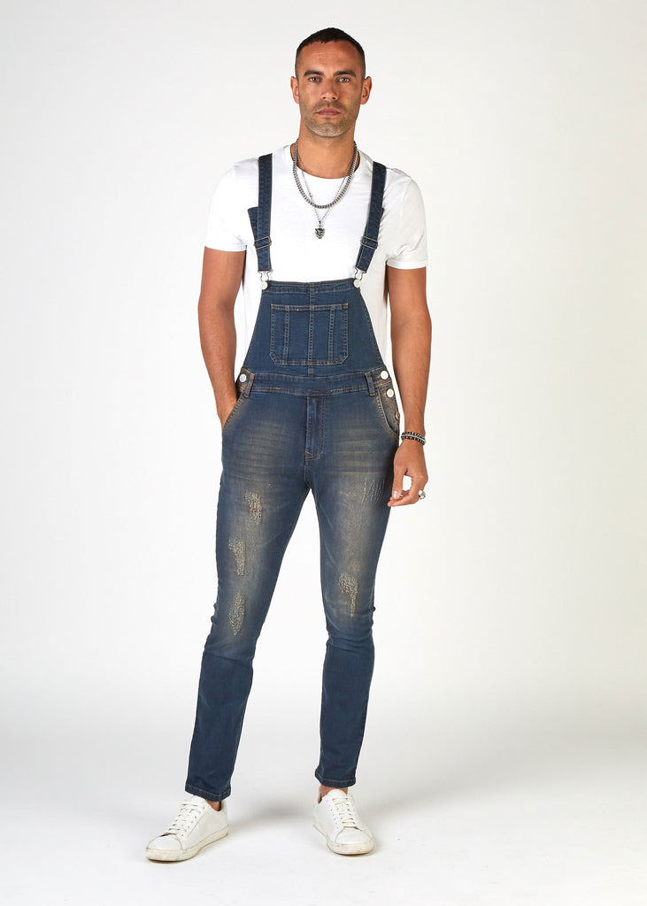 Full-front pose showing skinny fit style of dungarees with abrasions with hand in right pocket.