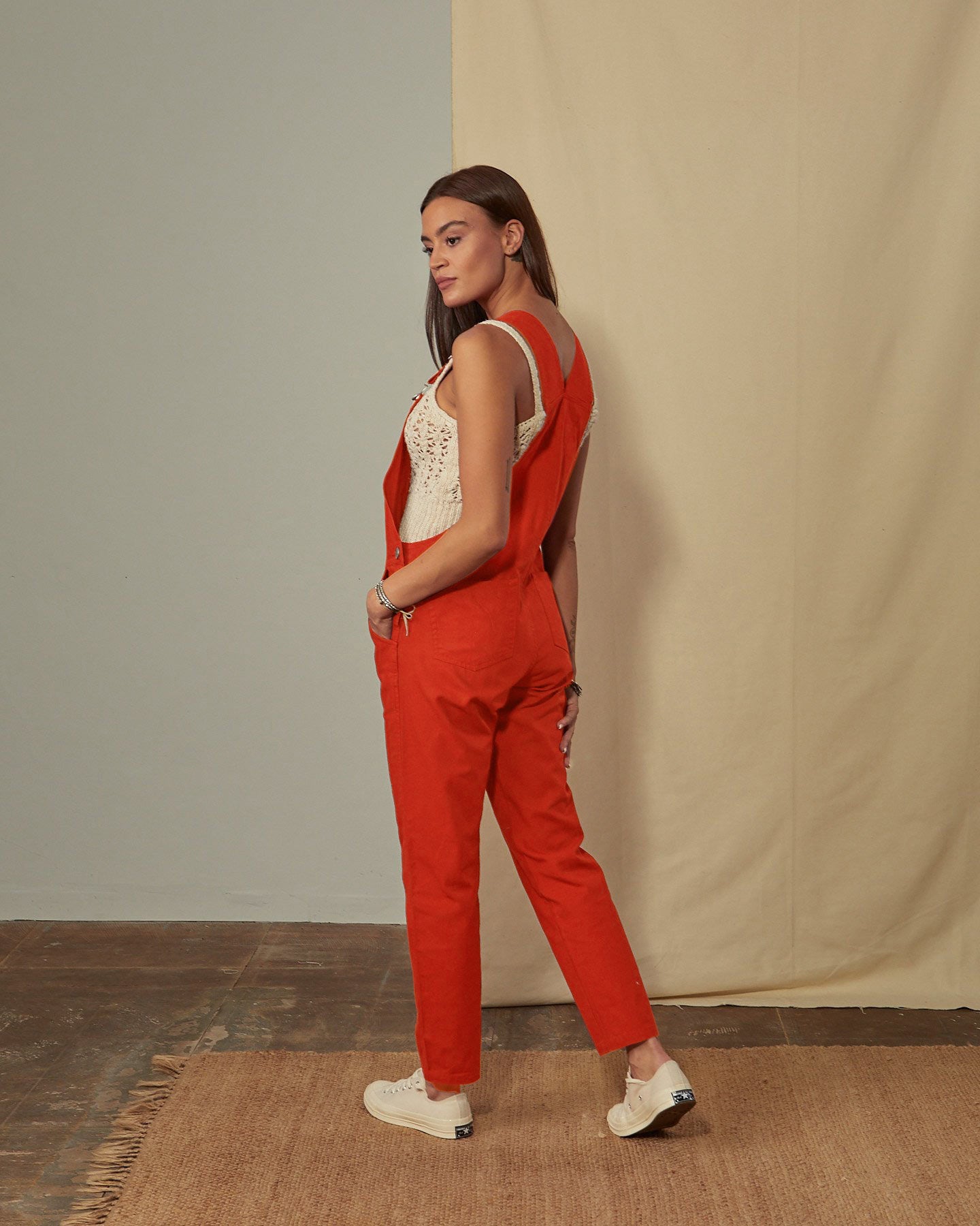 Full-length side view of model wearing Harper dark orange organic cotton dungarees showing back pockets and tapered leg.