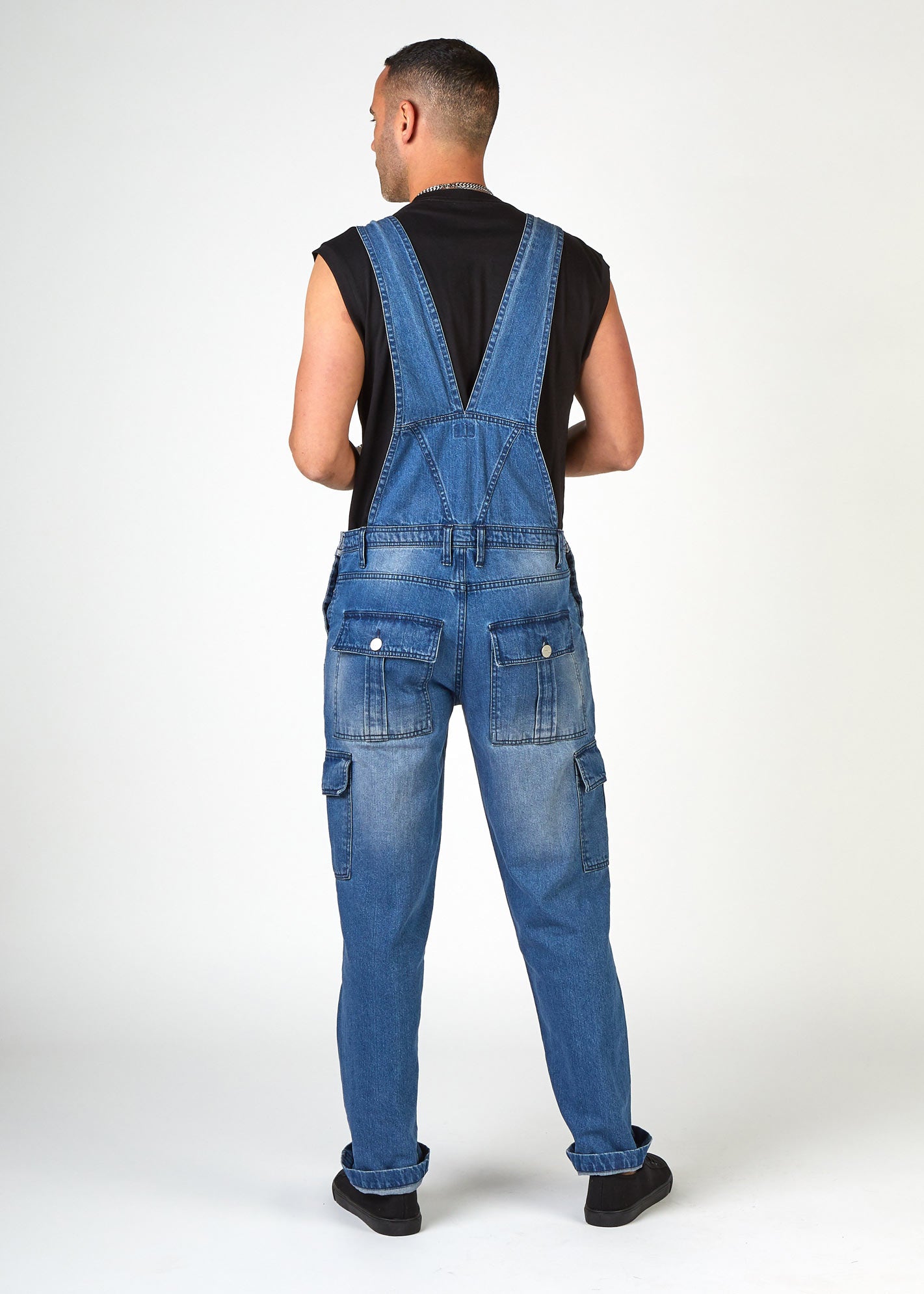 Back view of loose-fitting stonewash bib-overalls with clear view of back pockets, back strap, belt loops and denim detailing.