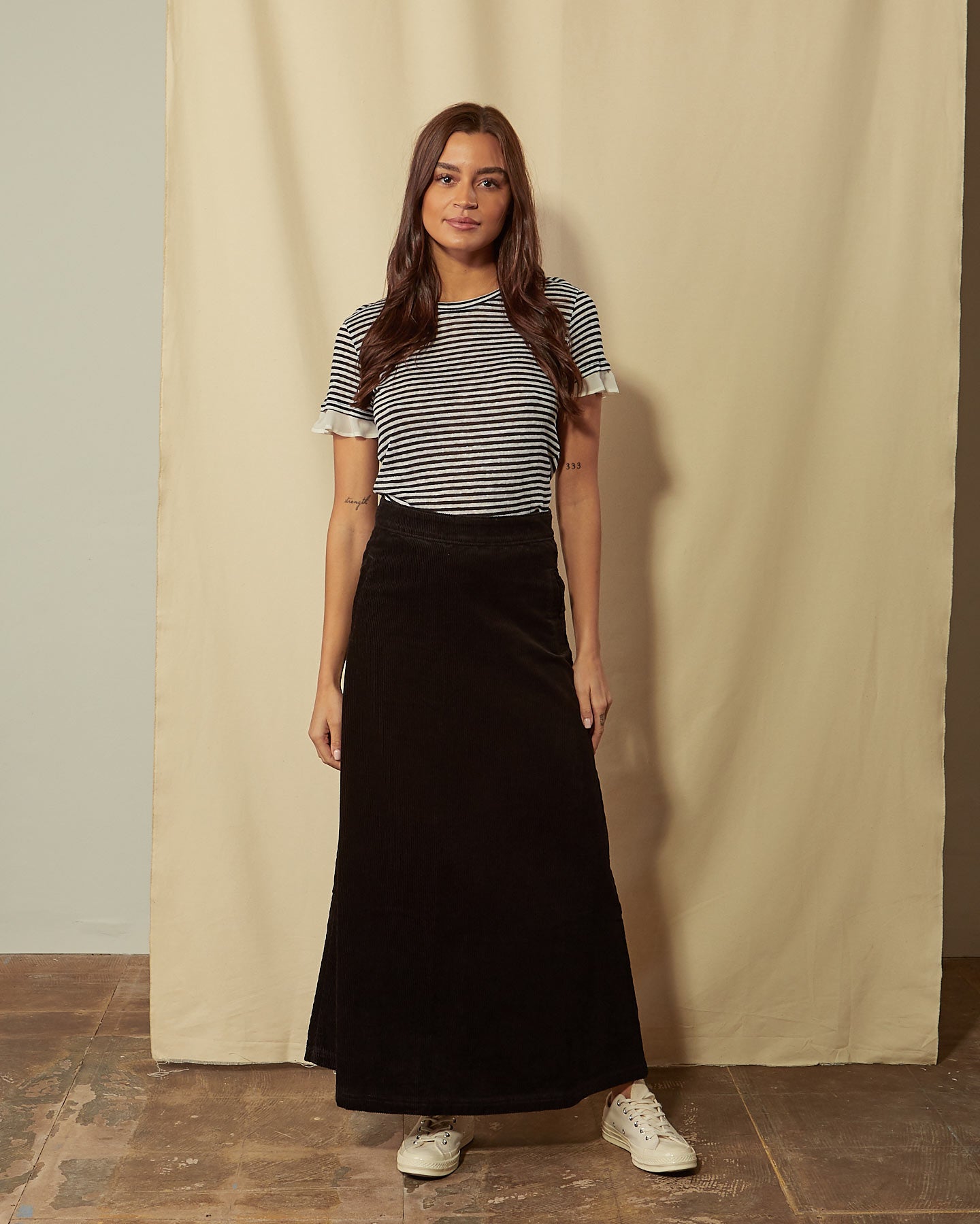 Full-length front view of model wearing Lottie black corduroy maxi-skirt demonstrating A-line silhouette.
