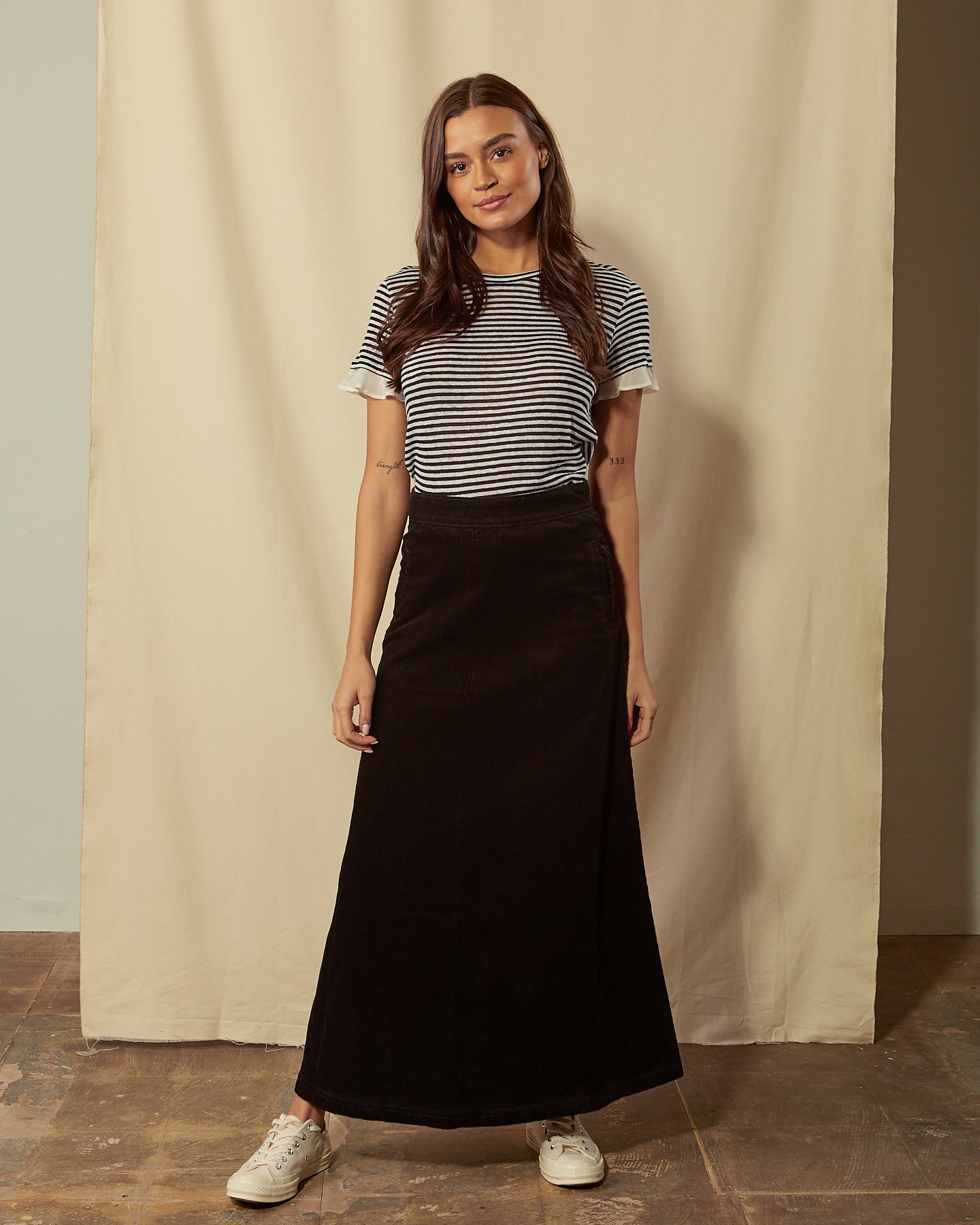 Full-length front view of model wearing Lottie black corduroy maxi-skirt demonstrating A-line silhouette.