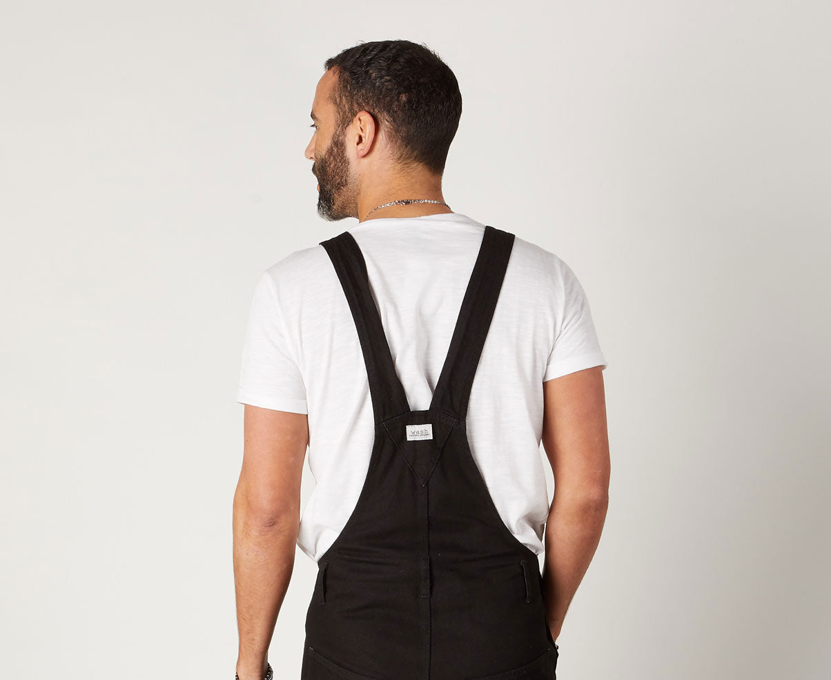 Top half view looking to left, wearing contemporary 'Maddox' black 10oz denim dungaree overalls with view of back straps.