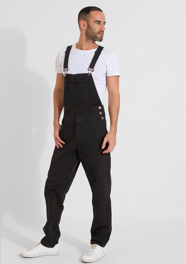 Front pose looking to left wearing black loose fit denim bib overalls.