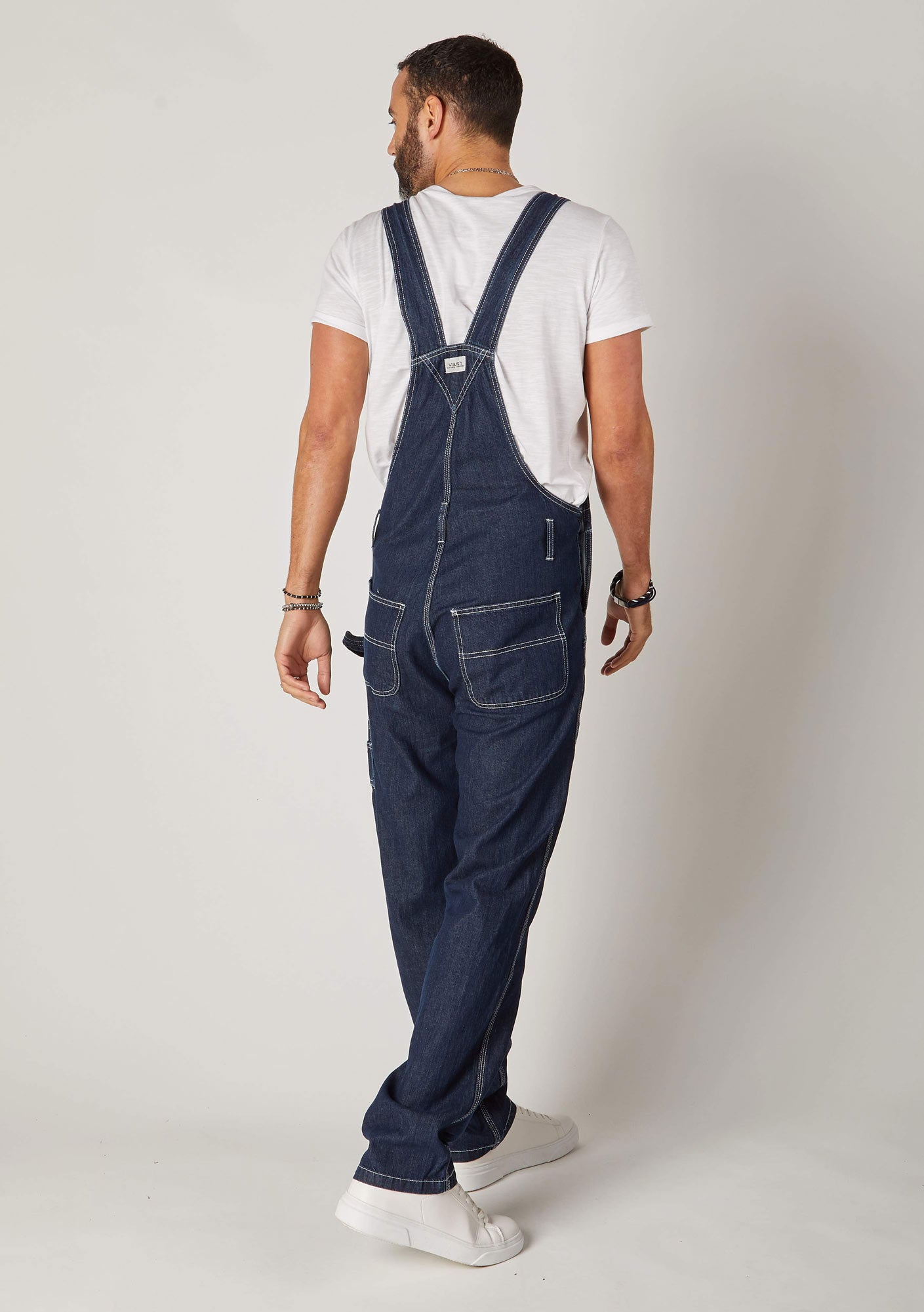 Full rear pose, angled to his right, wearing contemporary 'Maddox' blue 10oz denim dungaree overalls with view of back pockets and straps.
