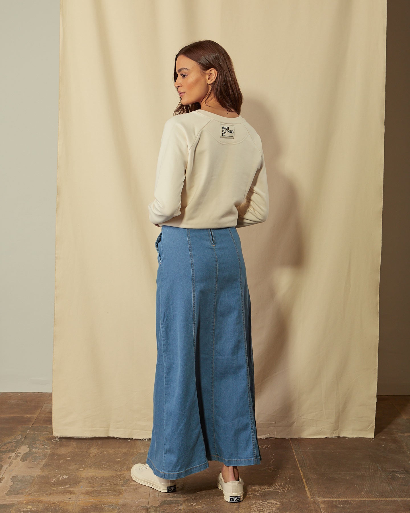 Angled back full-length shot of panelled denim maxi skirt showing side pocket, back zip and button fastening.