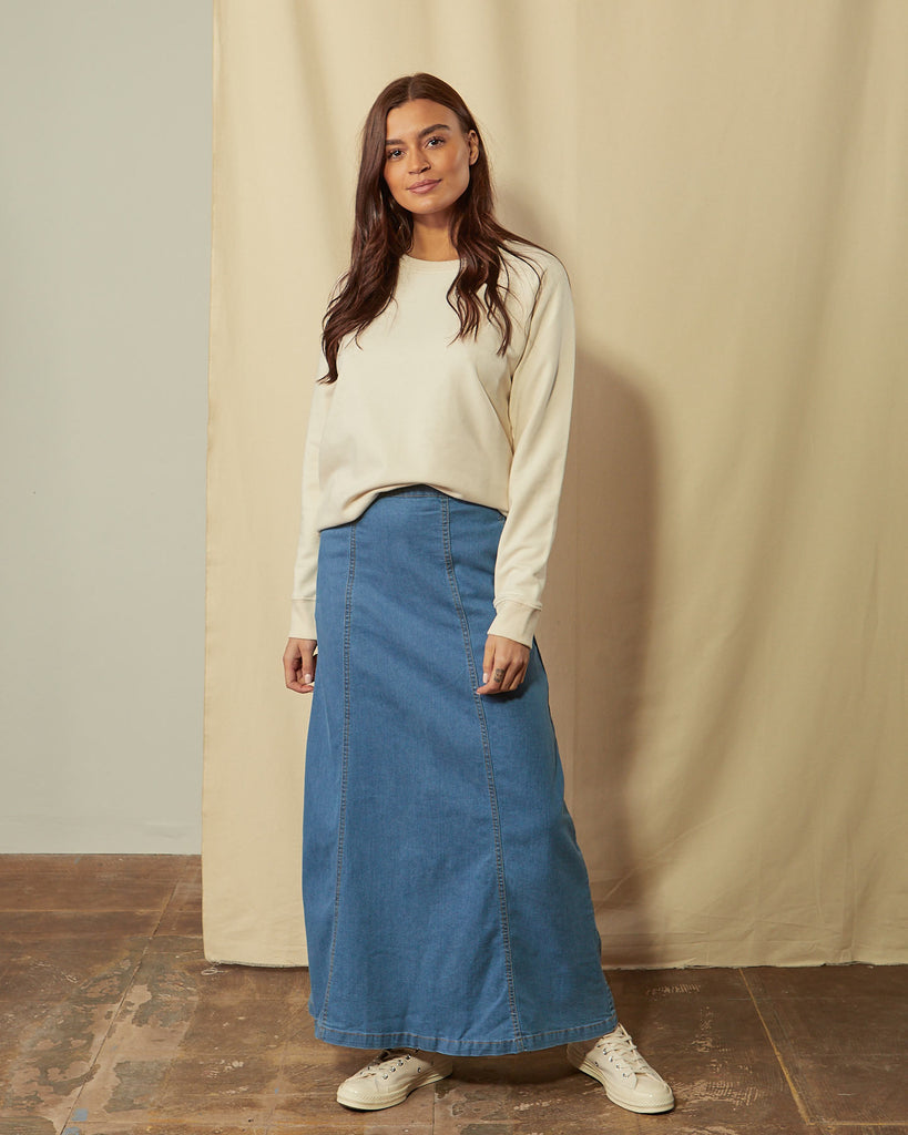 Front full-length shot model shot of panelled pale blue denim long skirt showing flared aspect.