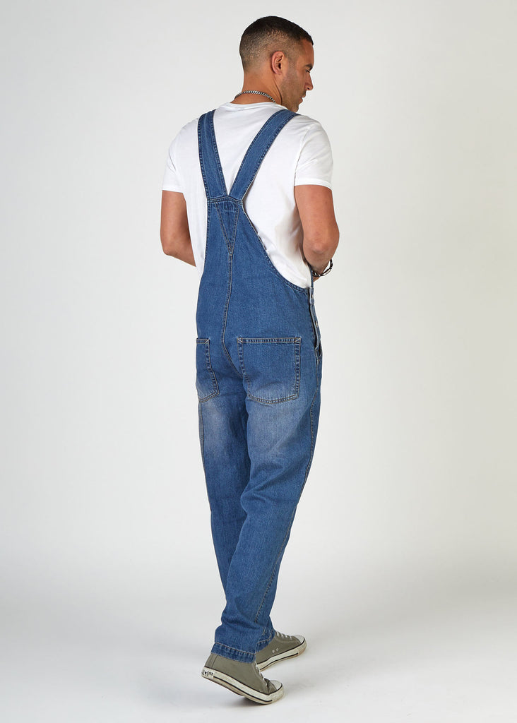 Back view twisting angled lightly to right, wearing classic-style stonewash bib-overalls with clear view of back pockets and back strap.