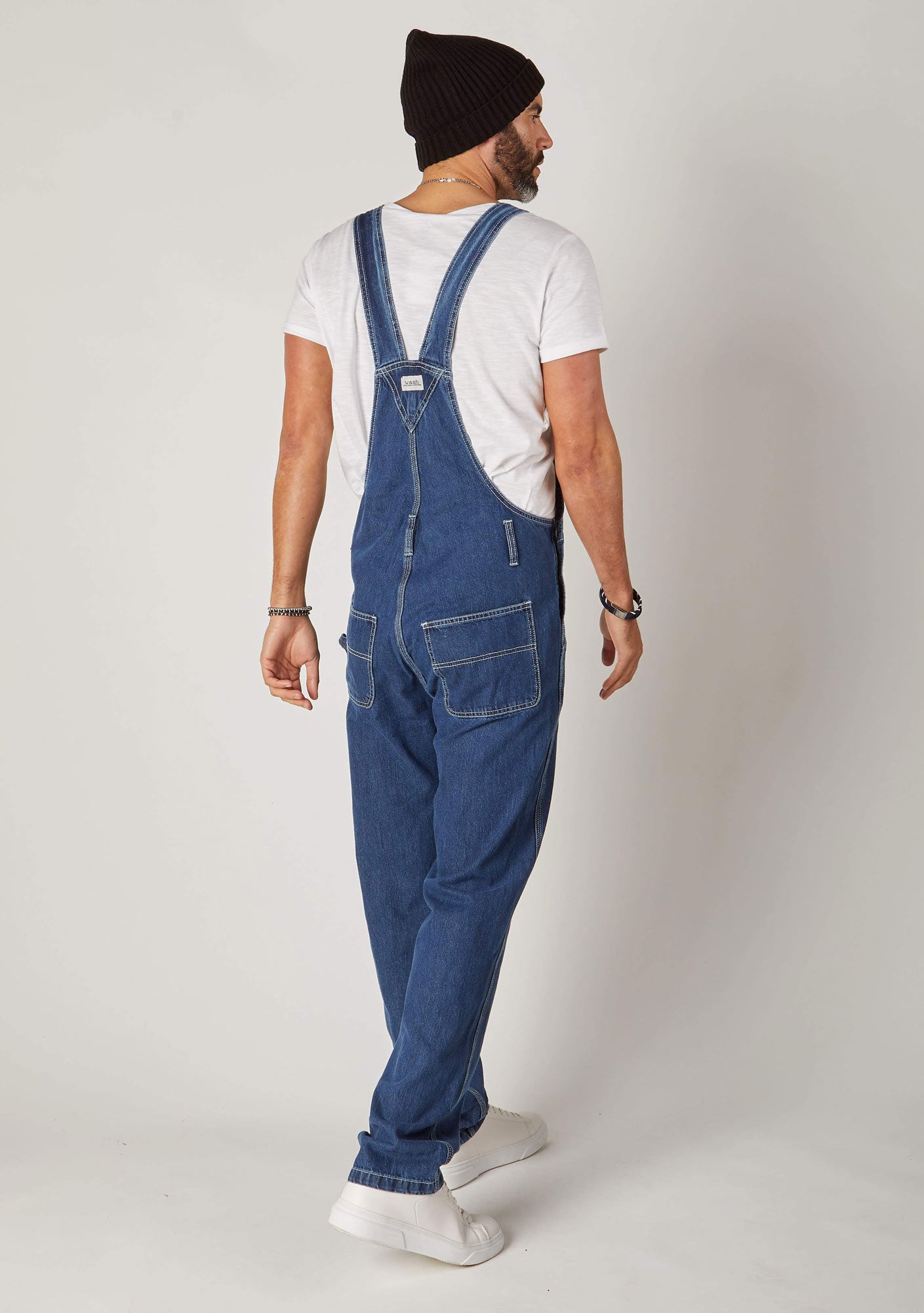 Full rear pose, angled to his right, wearing contemporary 'Maddox' stonewash 10oz denim dungaree overalls with view of back pockets and straps.
