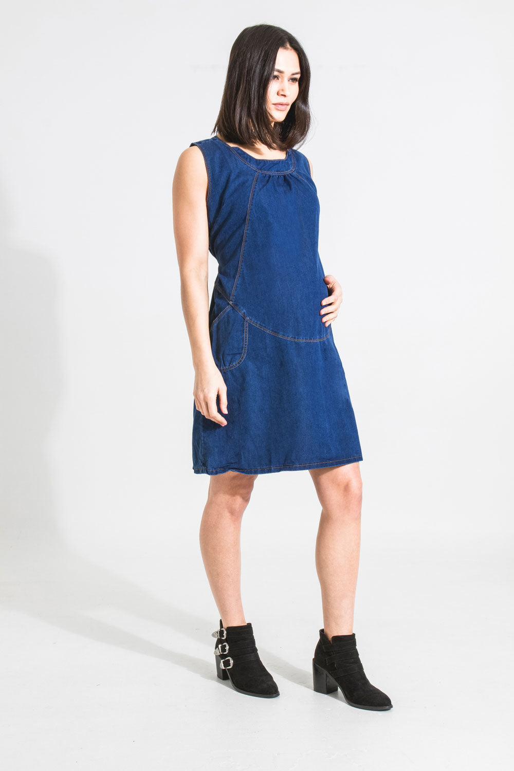 Full-length angled front view of Tasmin soft denim blue pinafore maternity dress.