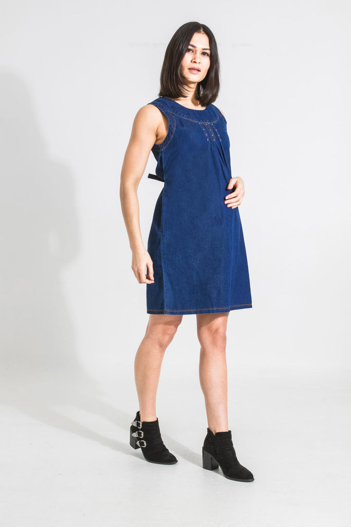 Full-length angled front view of Tina sleeveless denim maternity dress in blue showing attractive neckline detailing