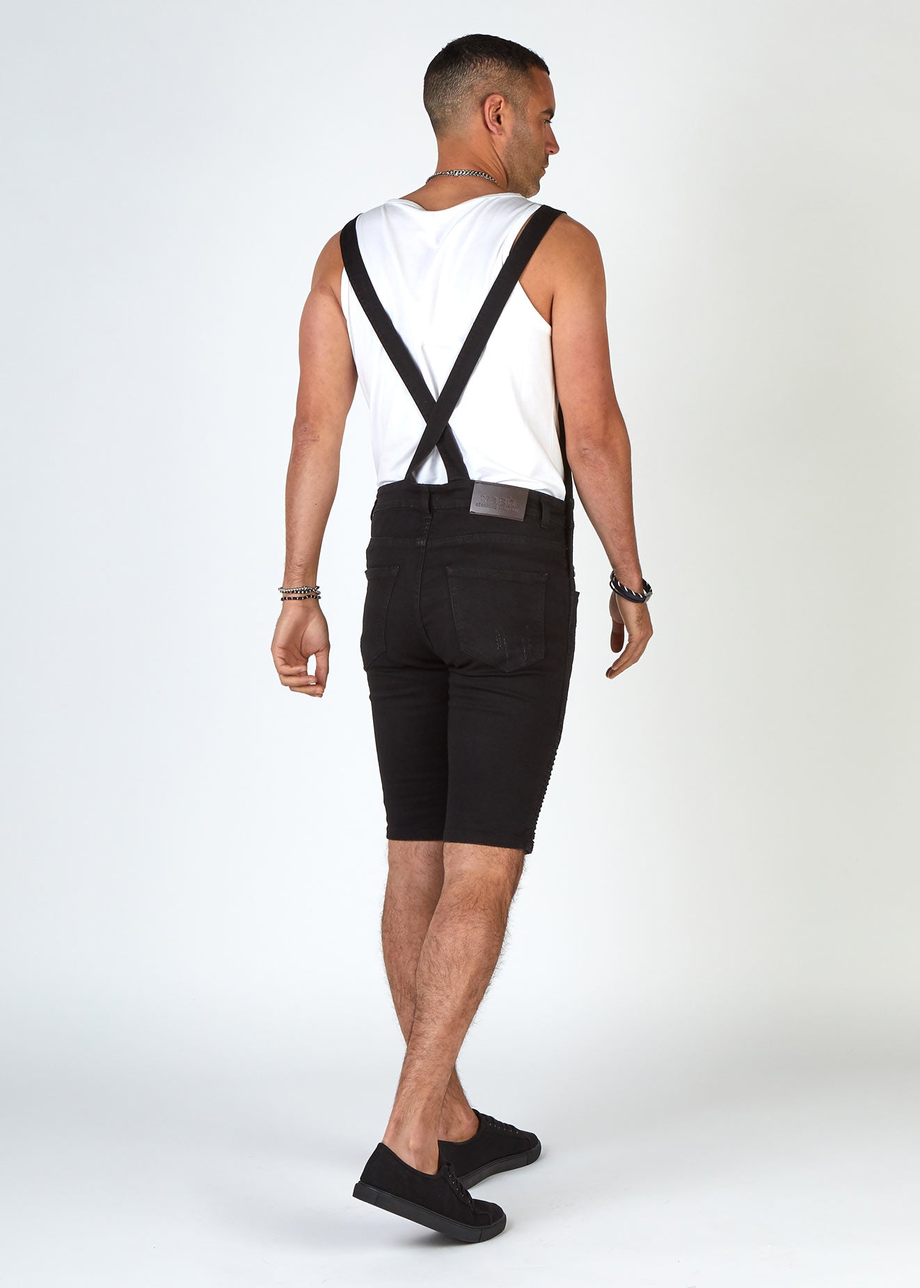 Rear pose to highlight slim overall straps that cross over at the back of Trafford biker dungaree shorts
