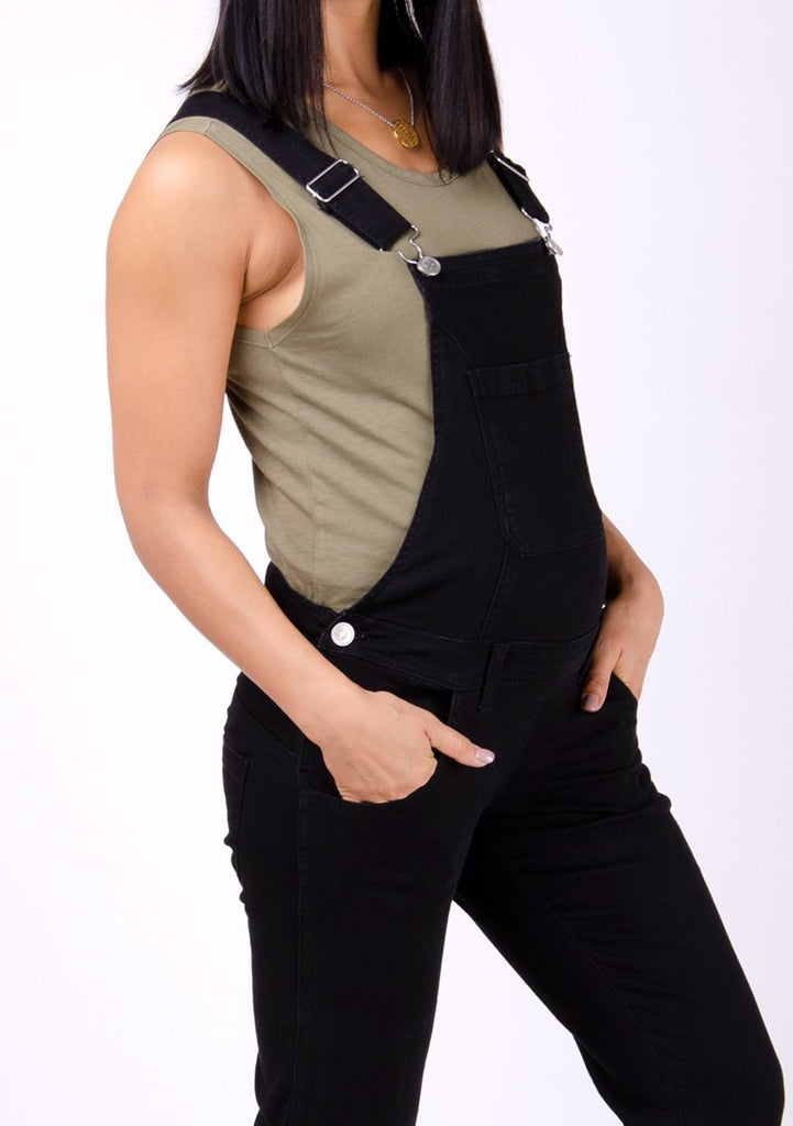 Two-thirds pose focussing on front pockets, side buttons and adjustable straps of black maternity overalls.