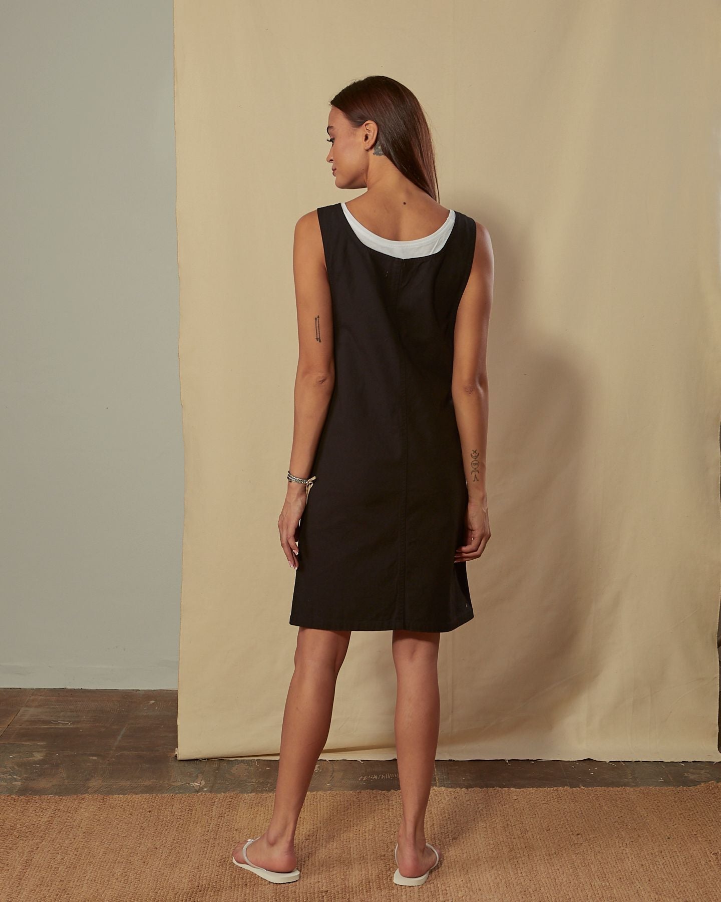 Full-length back view of model wearing Addie black organic cotton pinafore showing back scoop neck.
