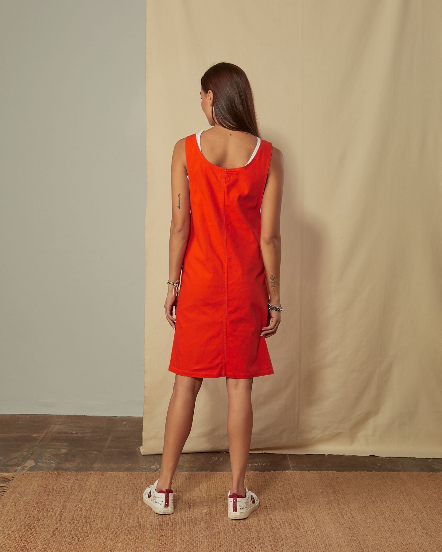 Full-length back view of model wearing Addie red organic cotton pinafore showing back scoop neck.