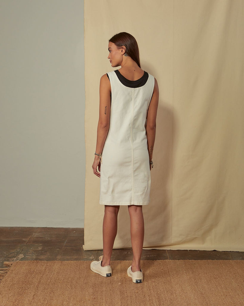 Full-length back view of model wearing Addie cream organic cotton pinafore showing back scoop neck.