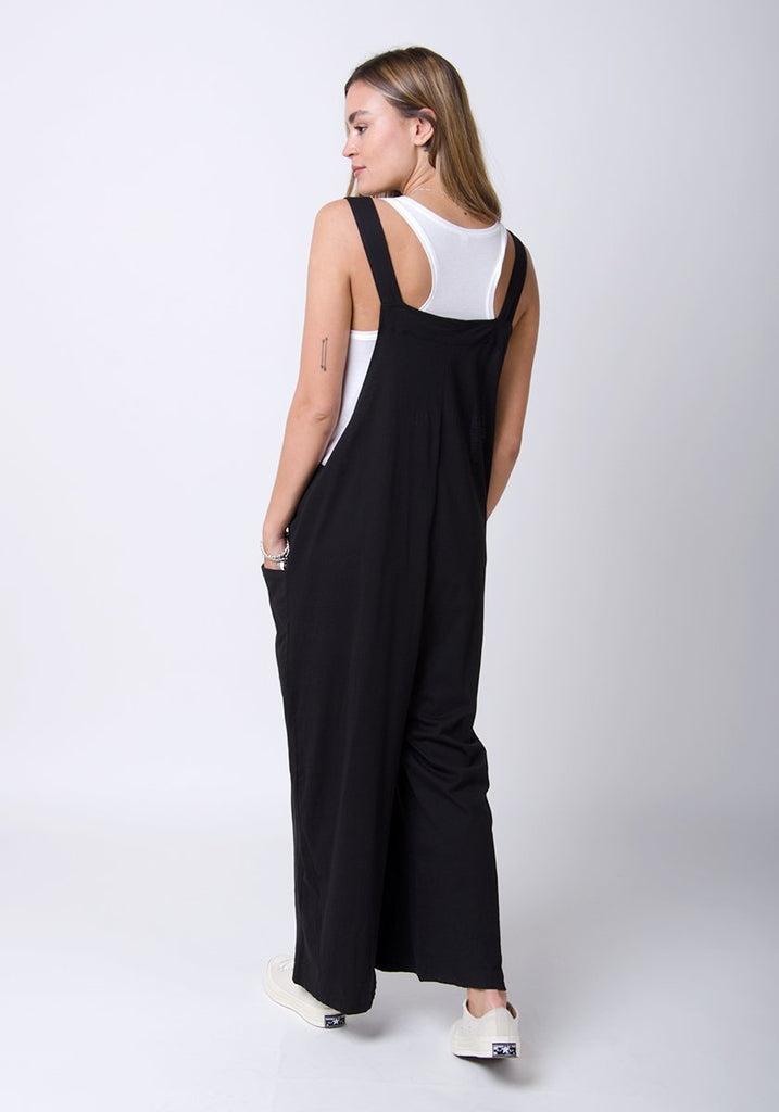 Rear full-length pose with Amber-style, black, cotton jersey, relaxed-fit dungarees showing adjustable straps.