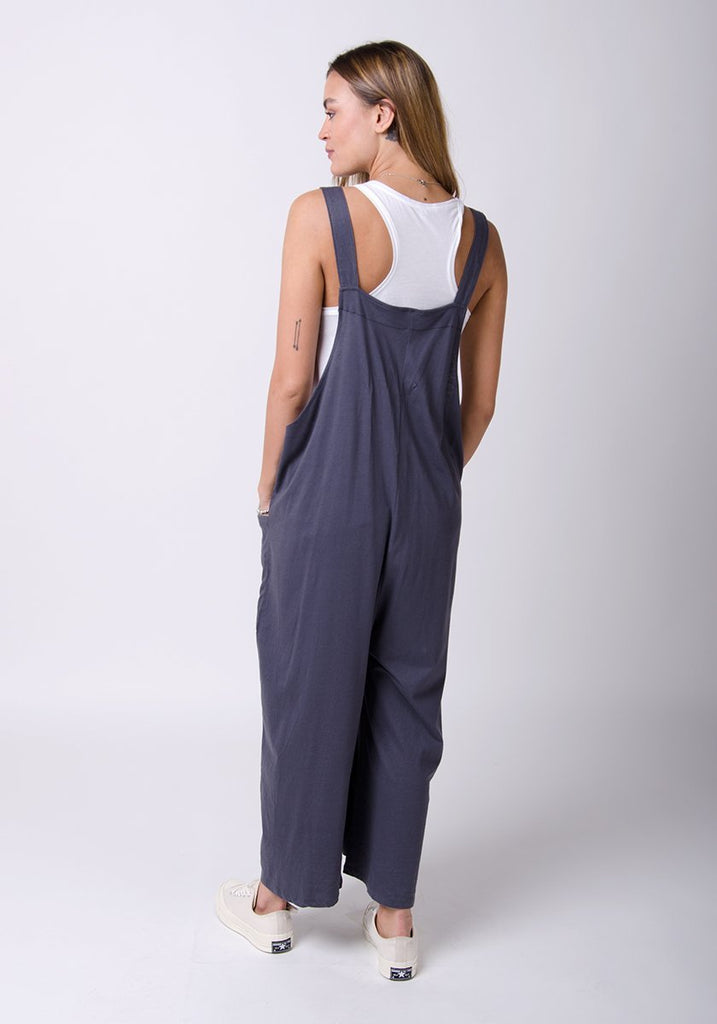 Rear full-length pose with Amber-style, charcoal, cotton jersey, relaxed-fit dungarees showing adjustable straps.
