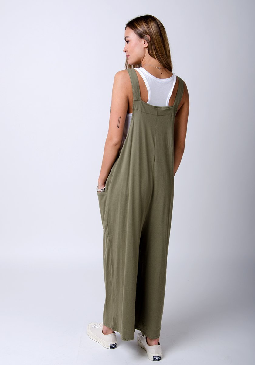 Rear full-length pose of super baggy, khaki-green, cotton jersey, dungarees showing adjustable straps.