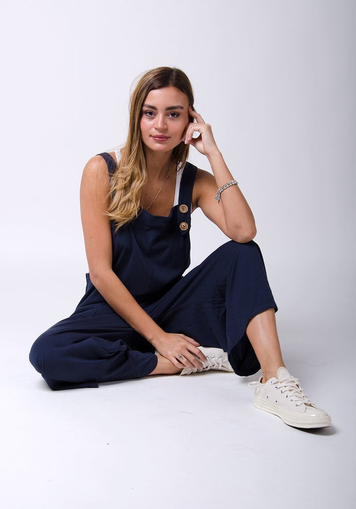Model sitting on floor in a relaxed pose wearing WASH brand, navy-blue, cotton jersey loose fit dungarees.