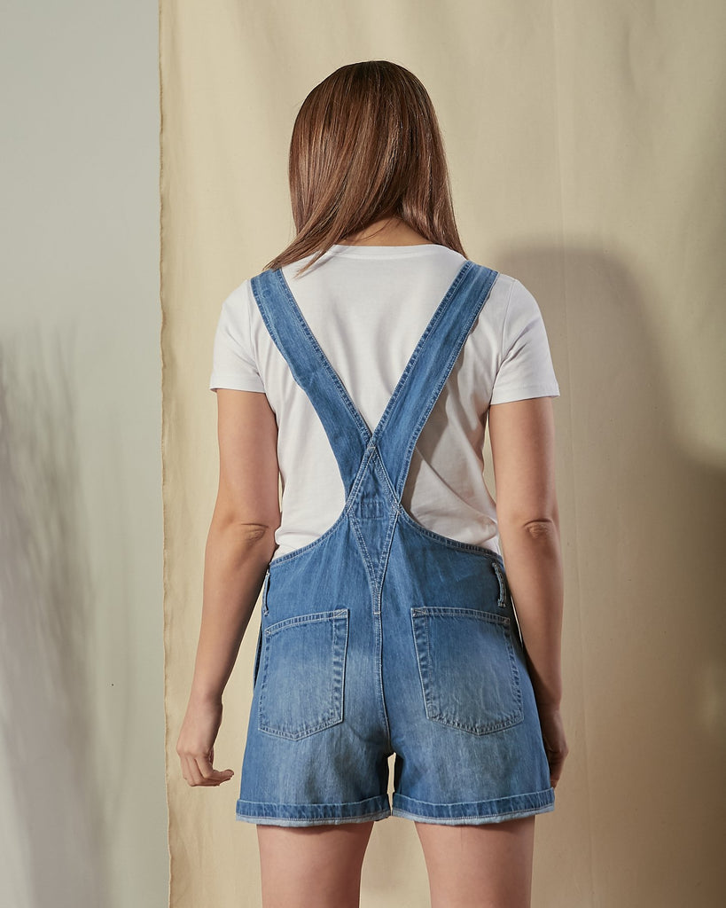 Two-thirds length back view of Ava blue denim dungaree shorts with view of back straps and back pockets.