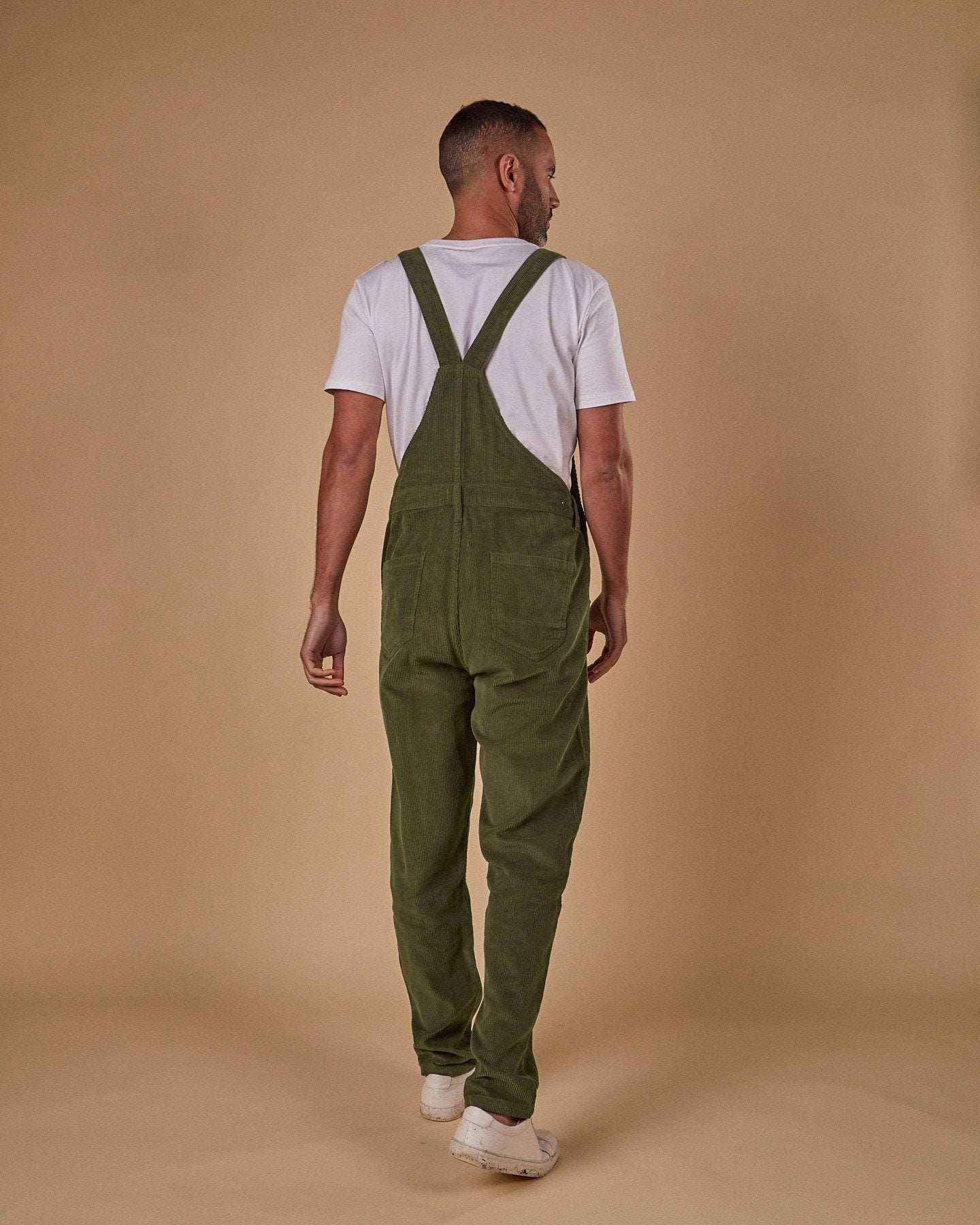 Full-length, back view of model wearing olive-green cord dungarees with clear view of back pockets and belt loops.