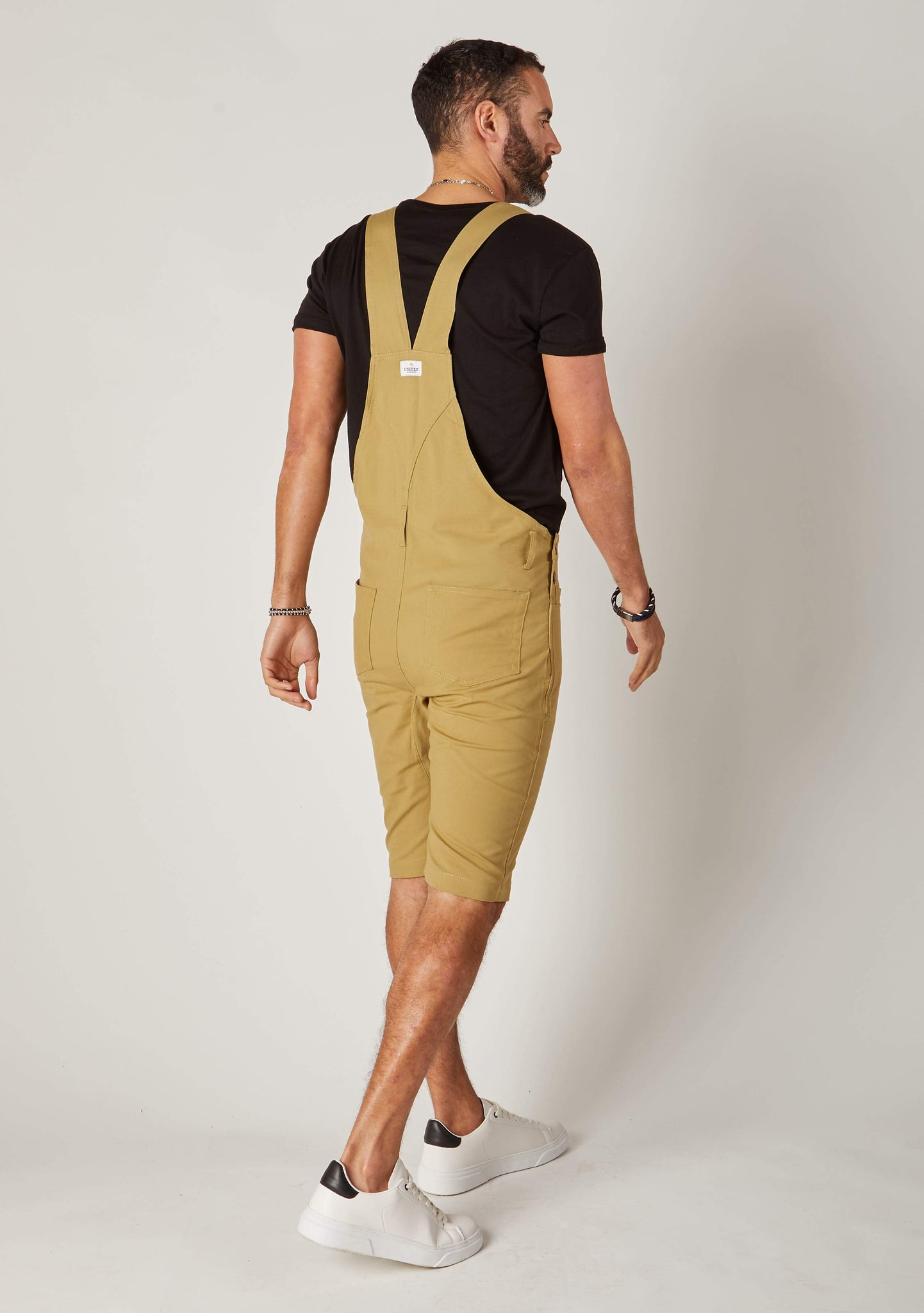 Rear-diagonal view of khaki, slim-fit cotton dungaree-shorts with clear view of cross straps and brand label.