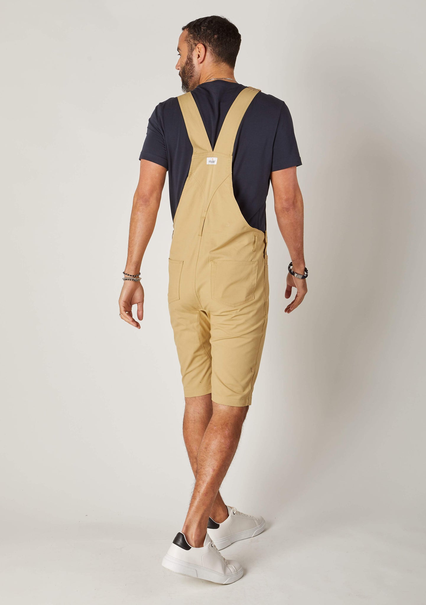Rear-diagonal view of sand, slim-fit cotton dungaree-shorts with clear view of cross straps and brand label.