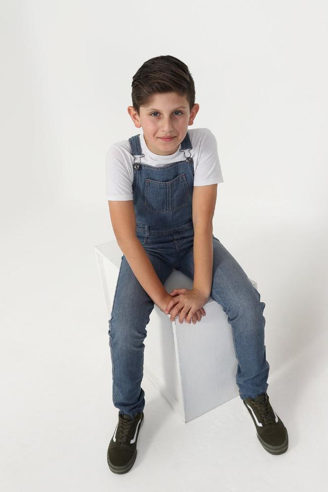 Full frontal of boy sitting on box wearing stylish kids bib-overalls.