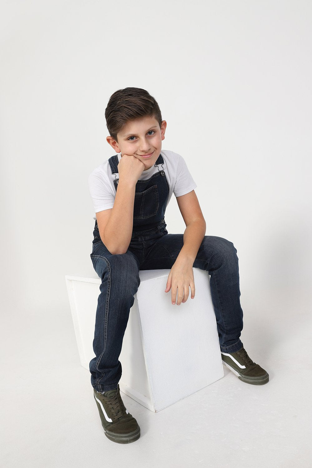 Boy slouching on box, wearing durable zip fly, machine washable kids overalls.