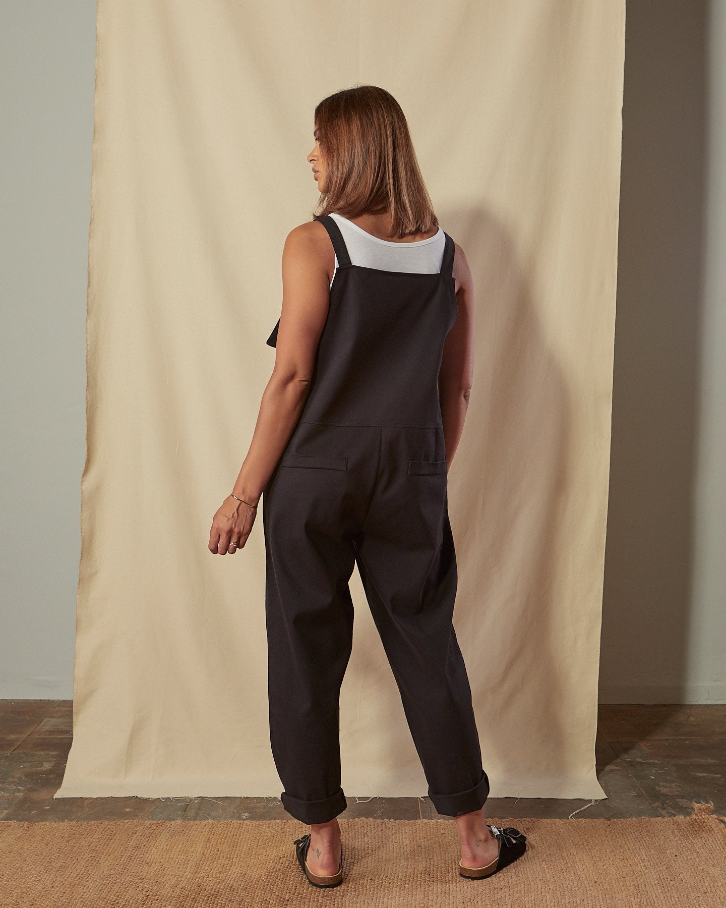 Full-length back view of Catherine black cotton twill dungarees with focus on mock pocket detailing.