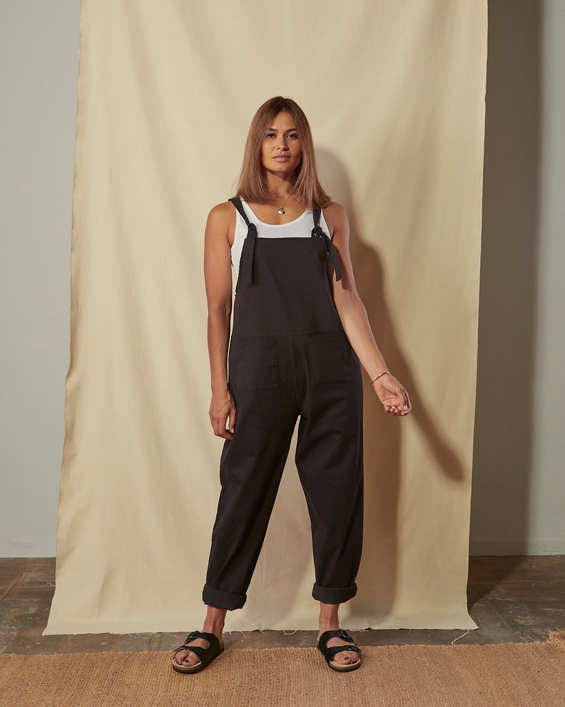 Full-length front view of Catherine black cotton twill dungarees with the legs slightly rolled up.
