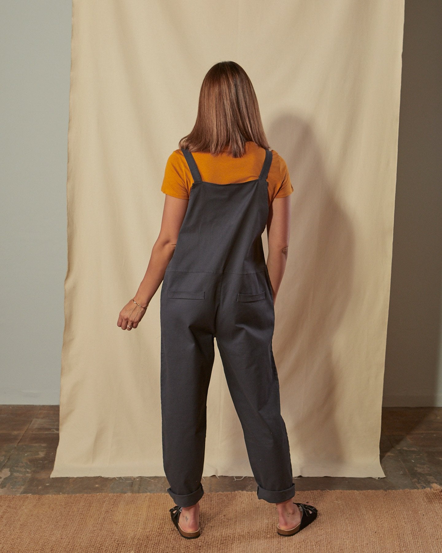 Full-length back view of Catherine dark grey cotton twill dungarees with focus on mock pocket detailing.