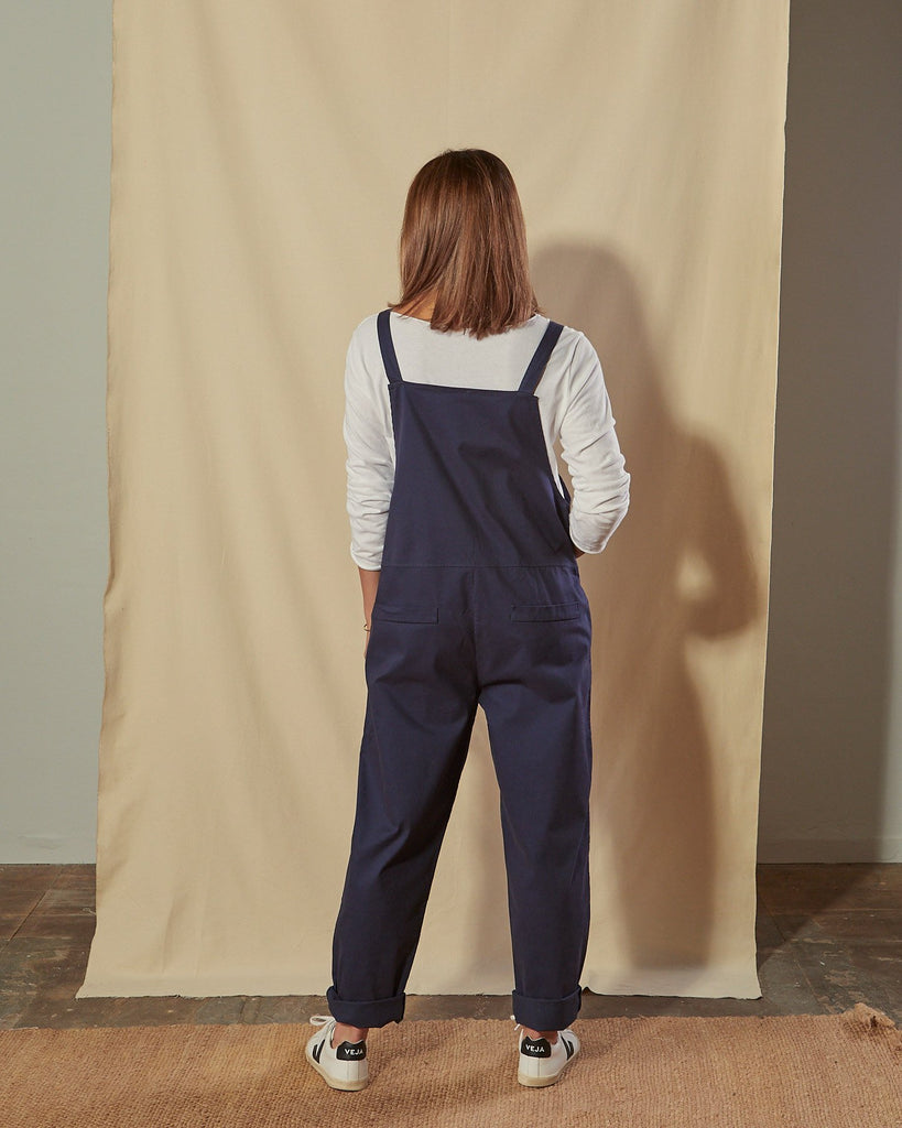 Full-length back view of Catherine navy blue cotton twill dungarees with focus on mock pocket detailing.
