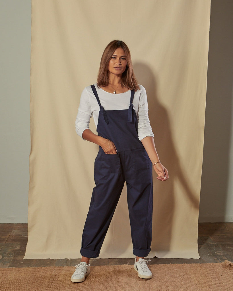 Full-length front view of model with hand in front pocket of Catherine navy blue cotton twill dungarees.