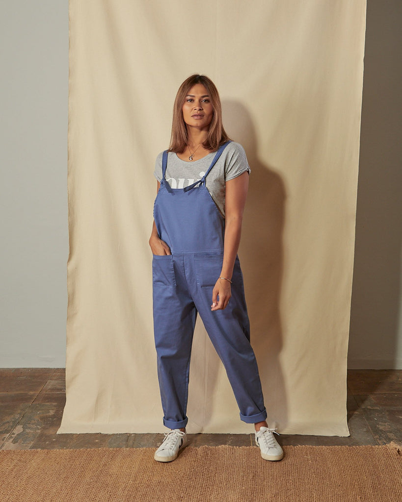 Full-length front view of model with hand in front pocket of Catherine muted blue cotton twill dungarees.