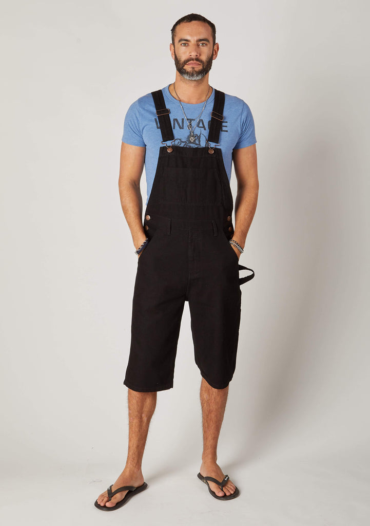 Full frontal pose wearing 'Chet' black denim bib overalls shorts.