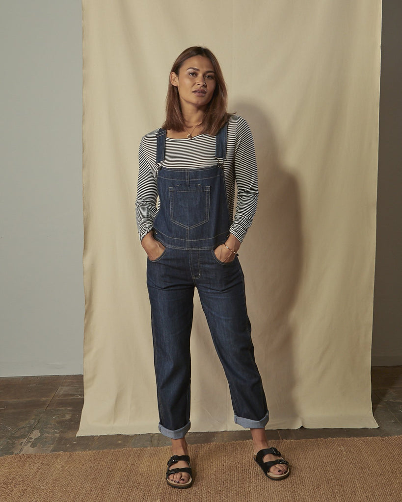 Full-length front shot of model with hands in front pockets of Dottie dark-wash ladies regular fit dungarees with view of turn-ups and bib pocket.